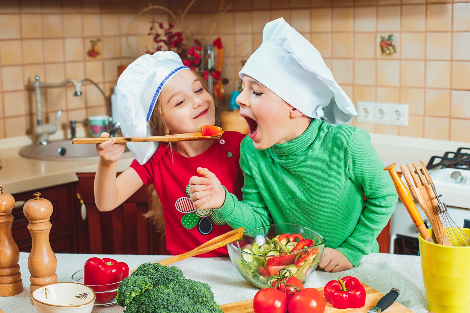 Szczęśliwa dwójka zabawnych dzieci przygotowuje w kuchni sałatkę ze świeżych warzyw
